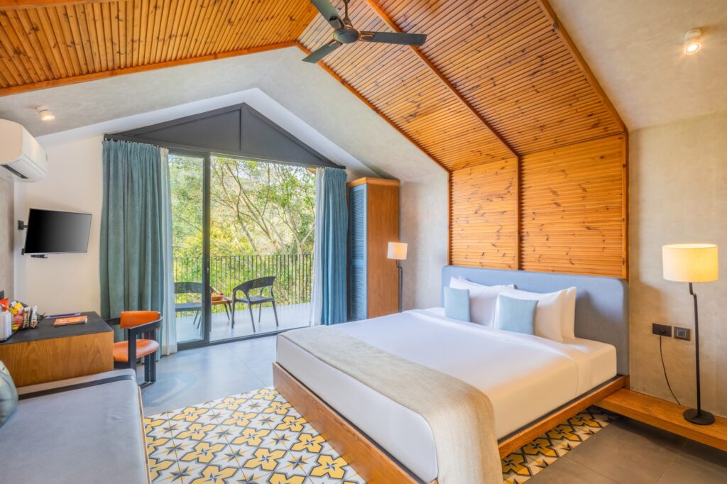 Modern bedroom featuring natural wood accents, comfortable bedding, and a view of lush greenery through glass doors.