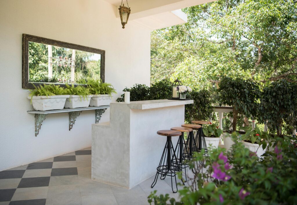 Stylish outdoor bar with stools and lush greenery, perfect for relaxation in a garden setting.